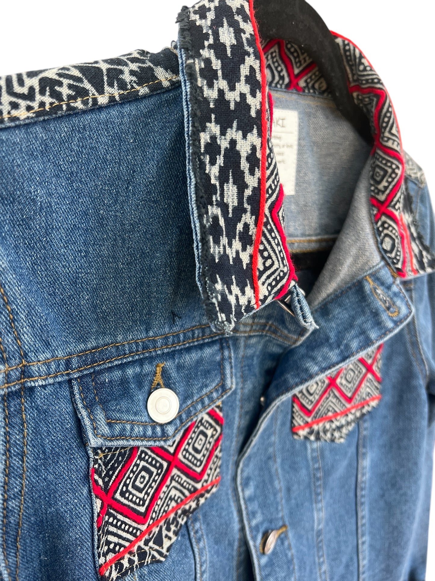 Jean jacket embellished with vibrant batik Hmong print textile on colar and front pockets combining traditional patterns with a modern denim style