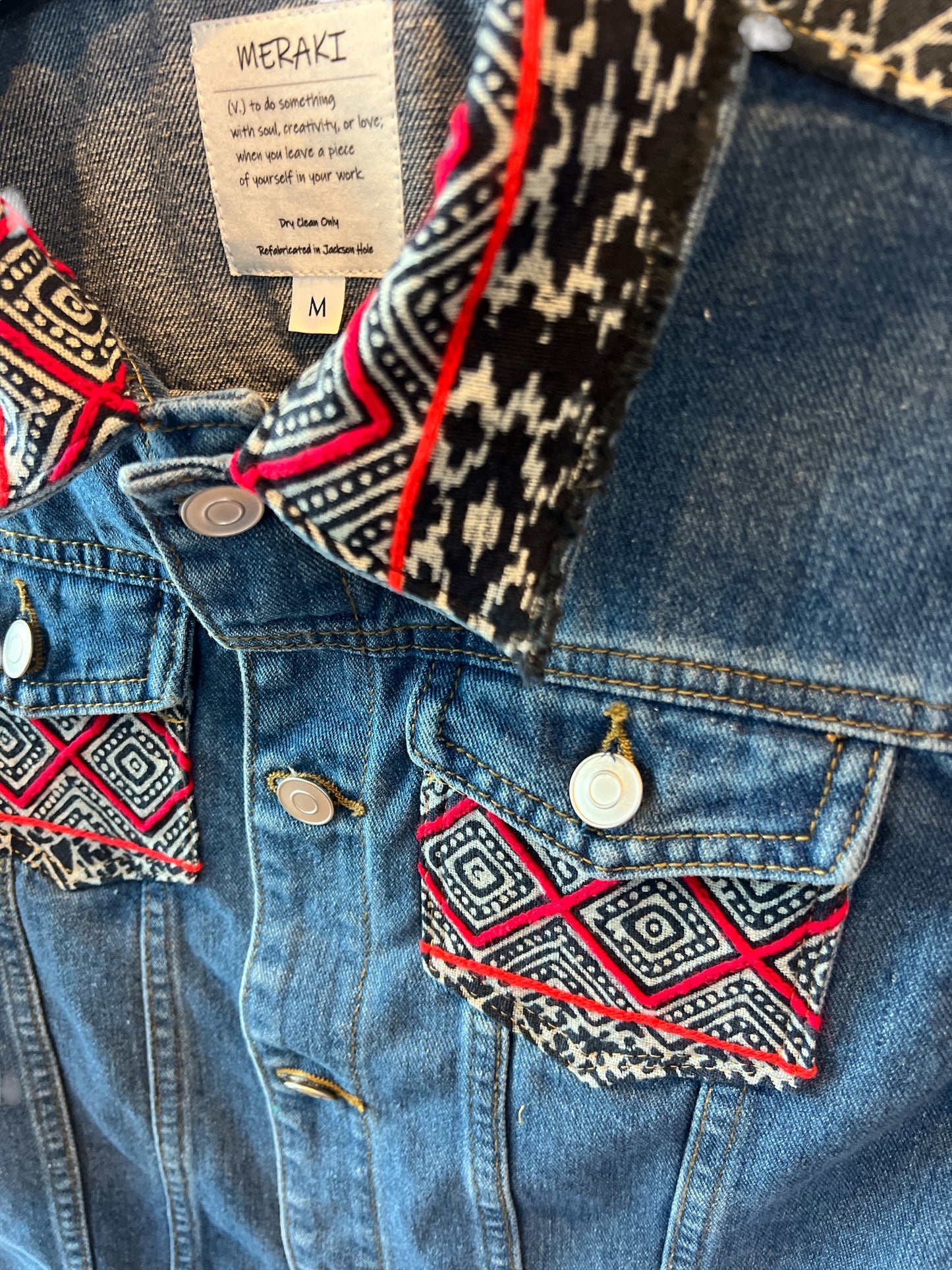 Jean jacket embellished with vibrant batik Hmong print textile on colar and front pockets combining traditional patterns with a modern denim style